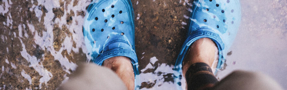 Elementarschutz Person steht in knöcheltiefem Wasser und trägt blaue Clogs.