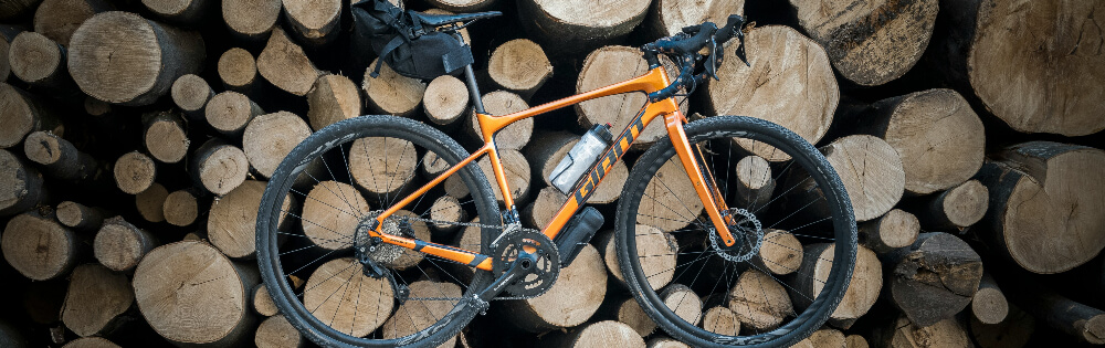 Fahrradversicherung Ein orangefarbenes Fahrrad lehnt an einem Stapel Holzstämme.