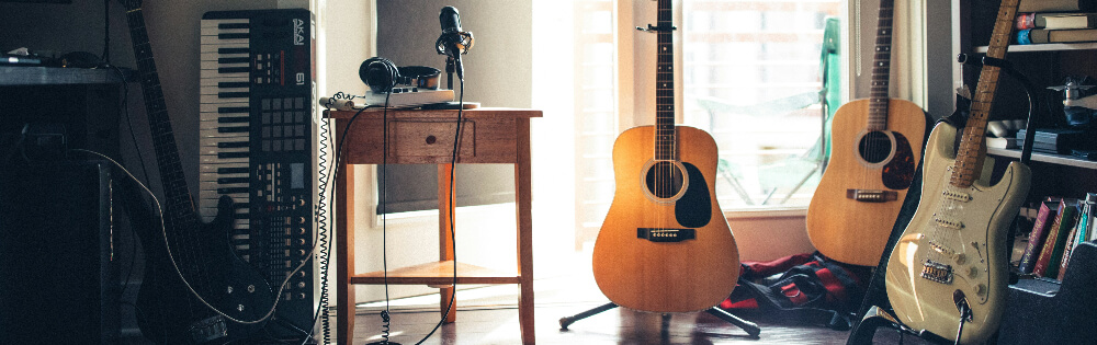 Raum mit Musikinstrumenten, darunter ein Keyboard, ein Tisch mit Kopfhörern und einem Mikrofon, zwei Akustikgitarren und eine E-Gitarre.